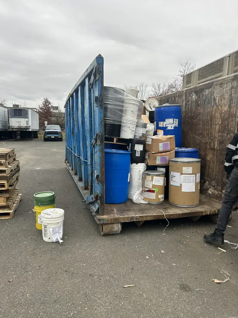 Blue dumpster and pallet stacked with industrial barrels and containers for safe hazardous waste disposal
