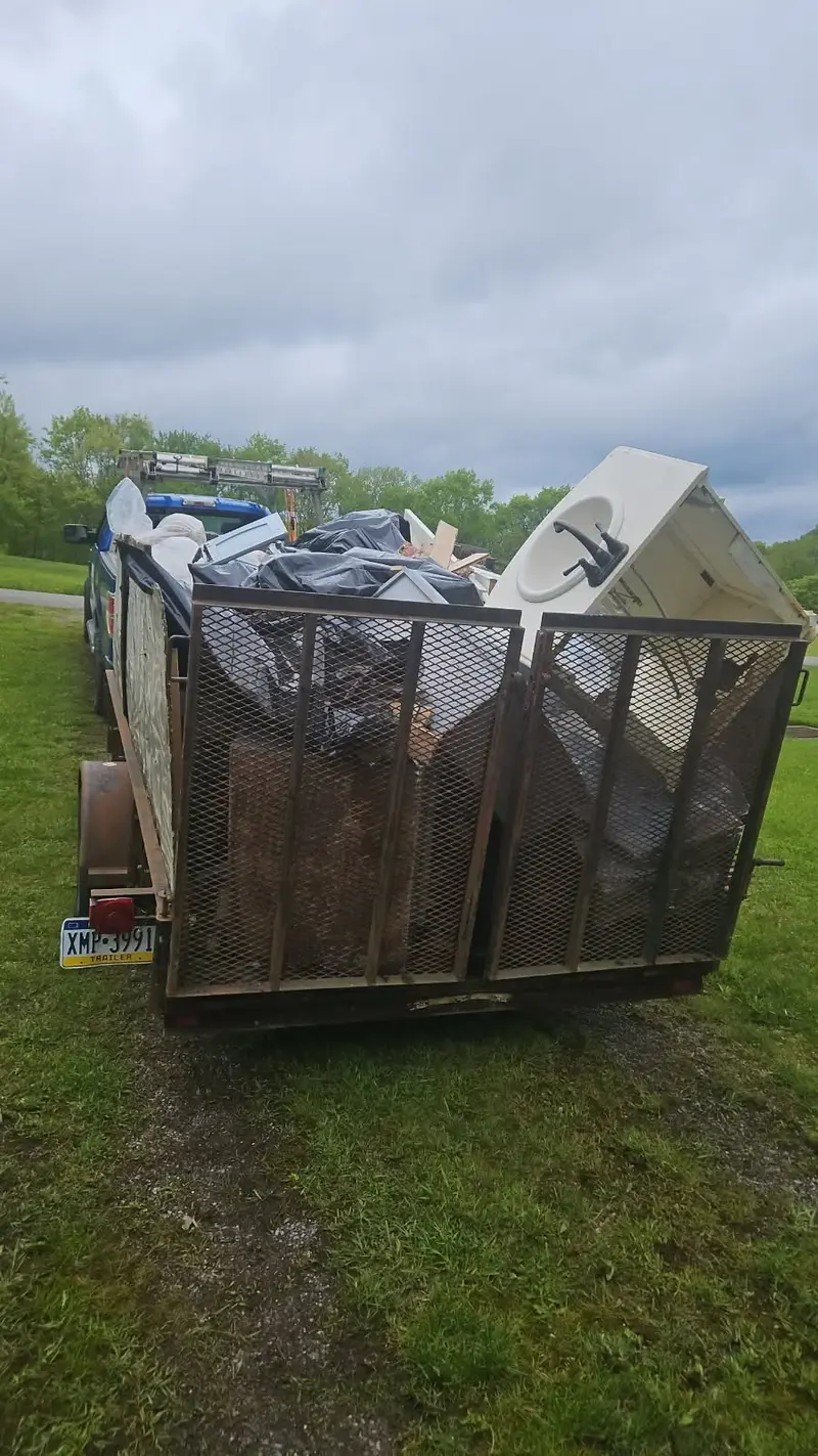 Trailer loaded with bulky junk including an old bathroom sink, furniture, and debris after a home renovation or cleanup