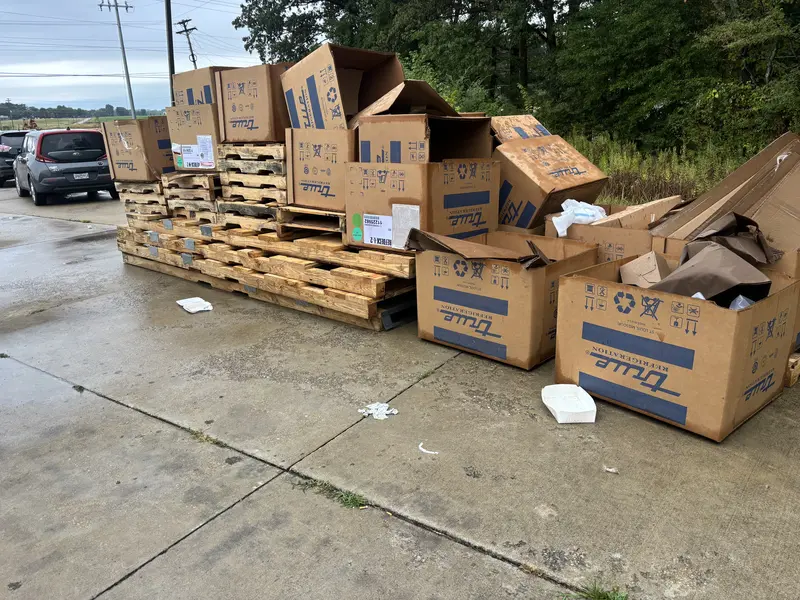 Illegal dumping site in rural area with piles of trash, furniture, and debris near trees and mountains